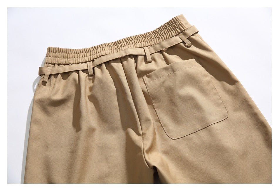 Close view of tan trousers with an elasticated waistband, belt loops, pleats and a large front patch pocket.