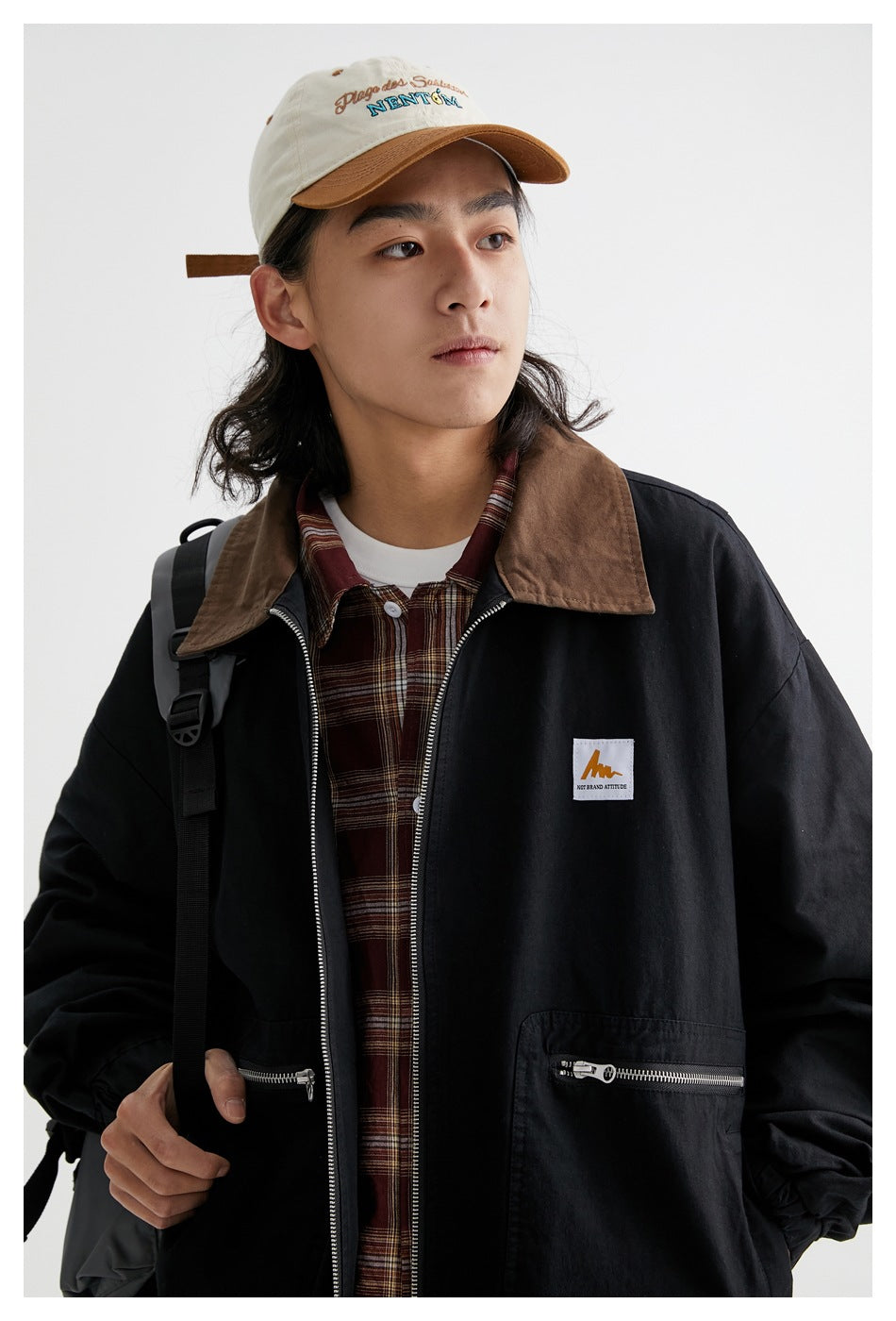 Close-up of a model wearing a black zip jacket with a brown collar, zip pockets and a small chest patch.