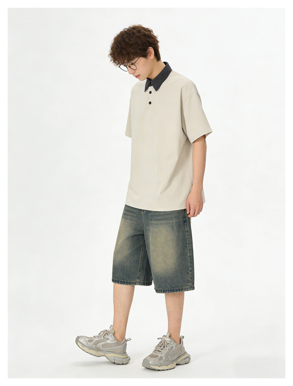 Model wearing a cream polo with black collar and buttons, faded denim shorts, and gray sneakers, shown from the front.