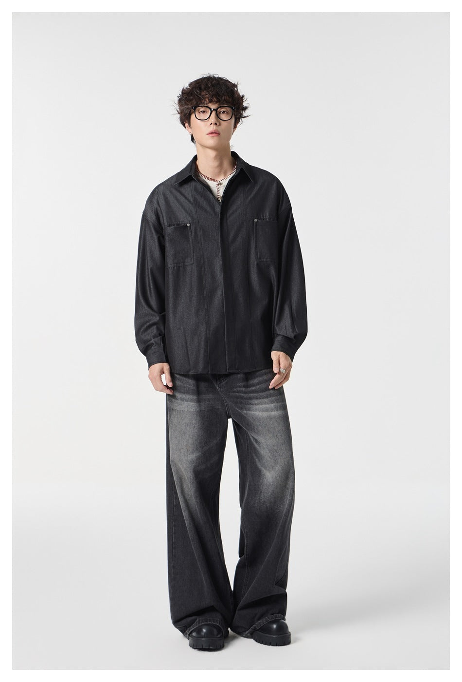 Full-length model wearing a dark charcoal button-up shirt with two chest pockets over a cream top and faded wide-leg jeans.