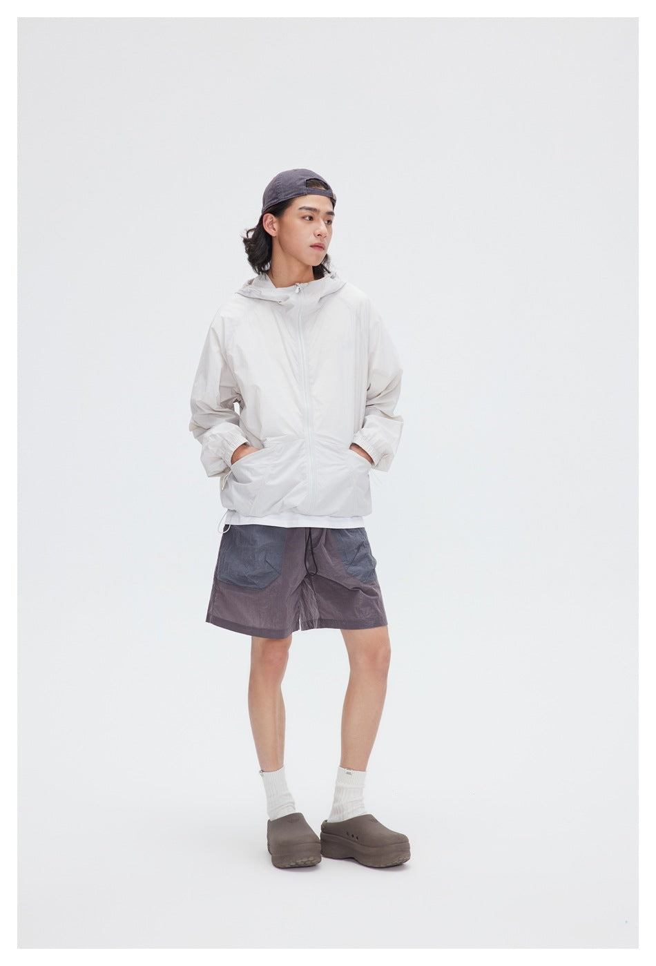 Model wearing a white hooded zip jacket with front pockets and dark gray shorts.