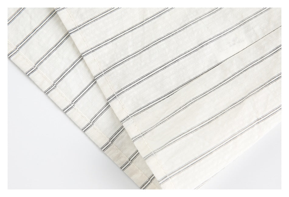 Close-up of the hem and folded edge of an ivory shirt with thin dark stripes.
