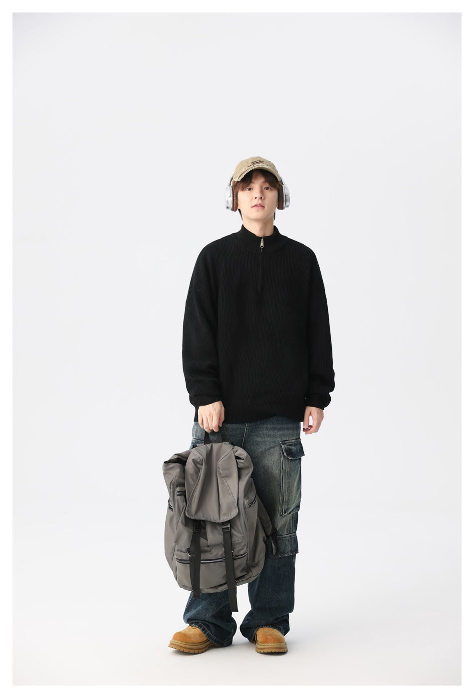 Model wearing a black ribbed quarter-zip sweater with dark jeans, holding a gray backpack.