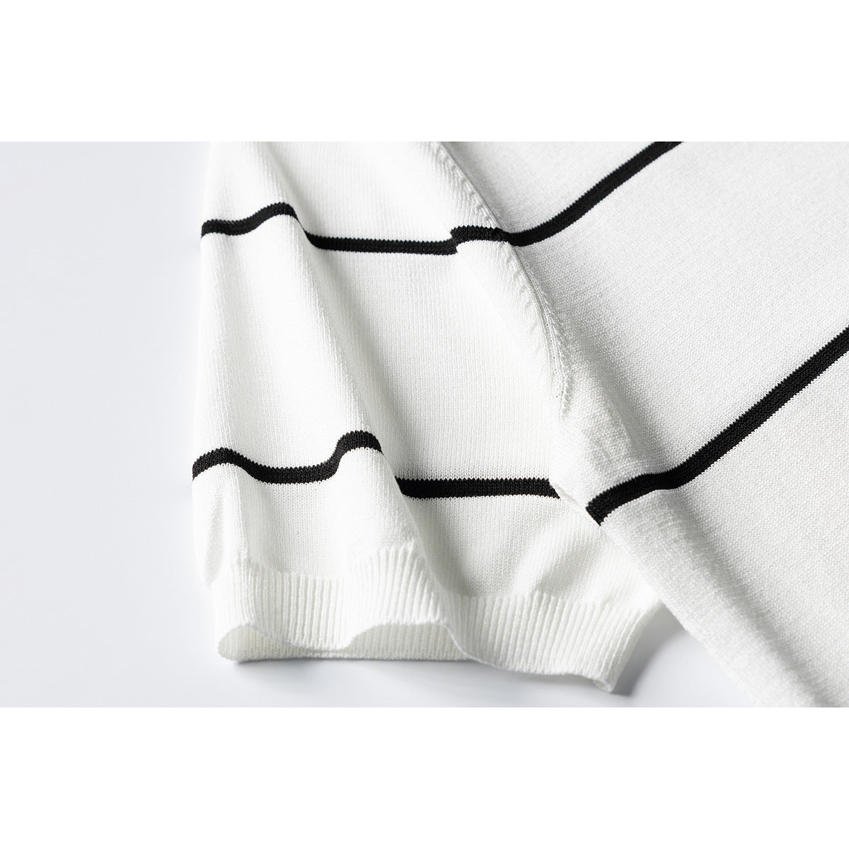 Close-up of an ivory knit top's black horizontal stripes, sleeve seam, and ribbed sleeve cuff.