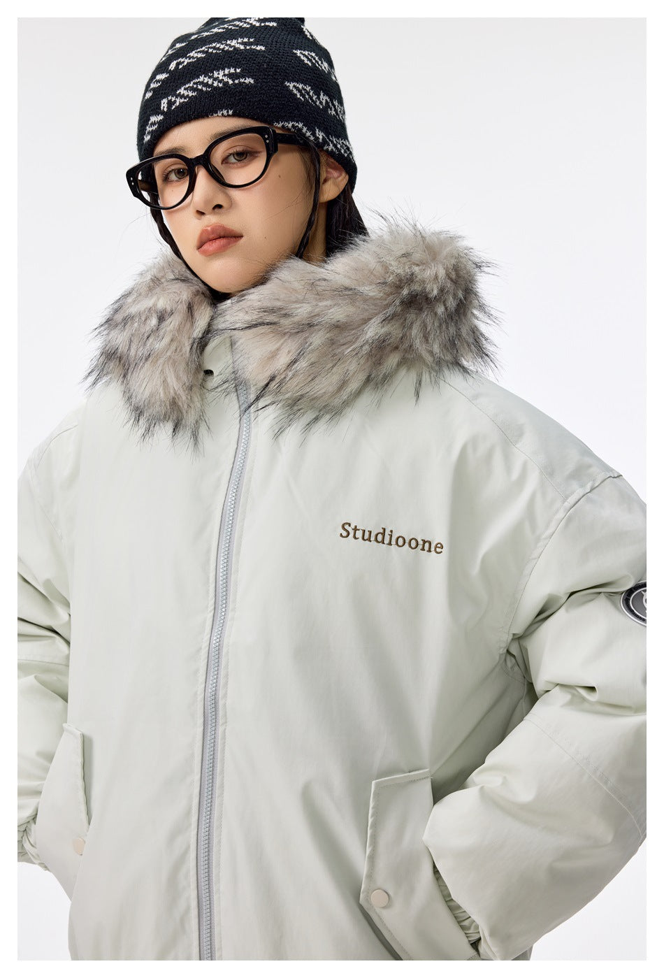 Close view of a model wearing a pale mint jacket with a gray faux-fur hood and front zipper.