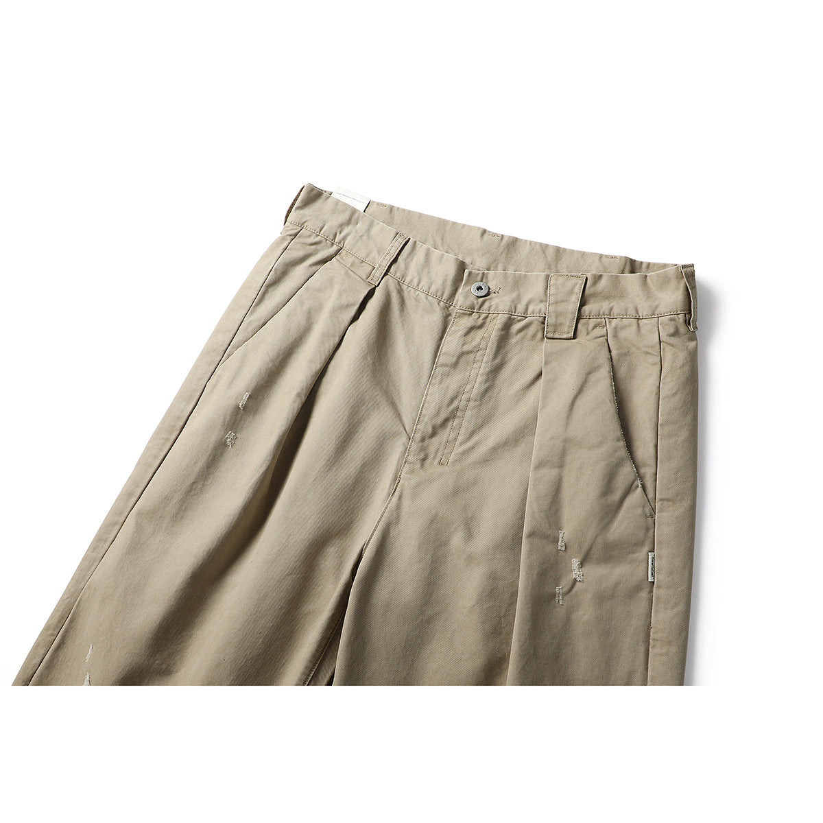 Close view of beige pleated trousers showing the waistband, button, pockets and small distressed details.