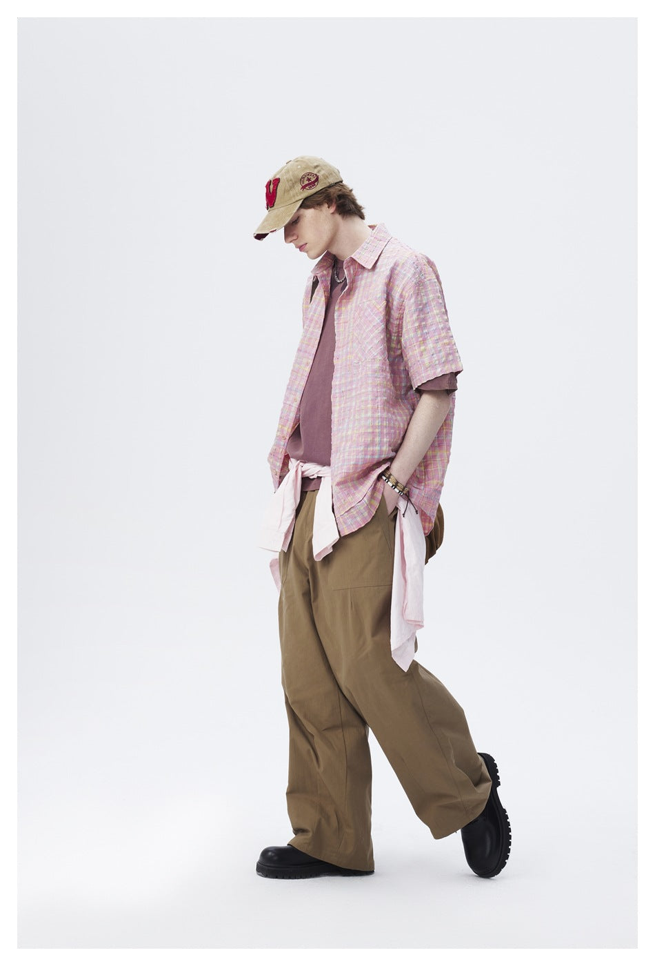 Side view of a model wearing a pastel pink plaid short-sleeve shirt and loose olive trousers.