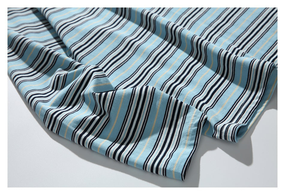 Close-up of the light blue shirt's black, white, and tan stripes, showing folds and a stitched hem.