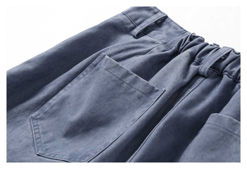 Close-up of blue-gray trousers showing the elastic waist, belt loops, and large patch pocket.