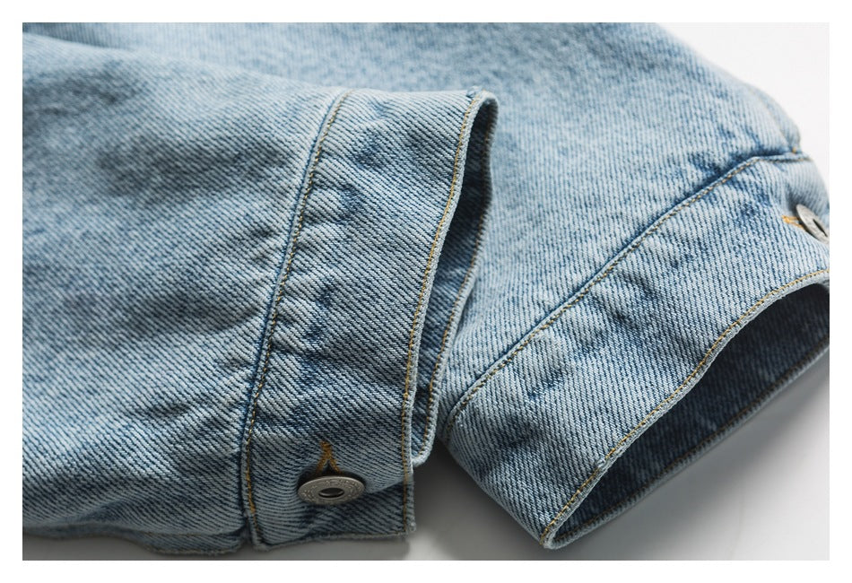 Close-up of a denim jacket sleeve cuff with a metal button and contrast stitching.