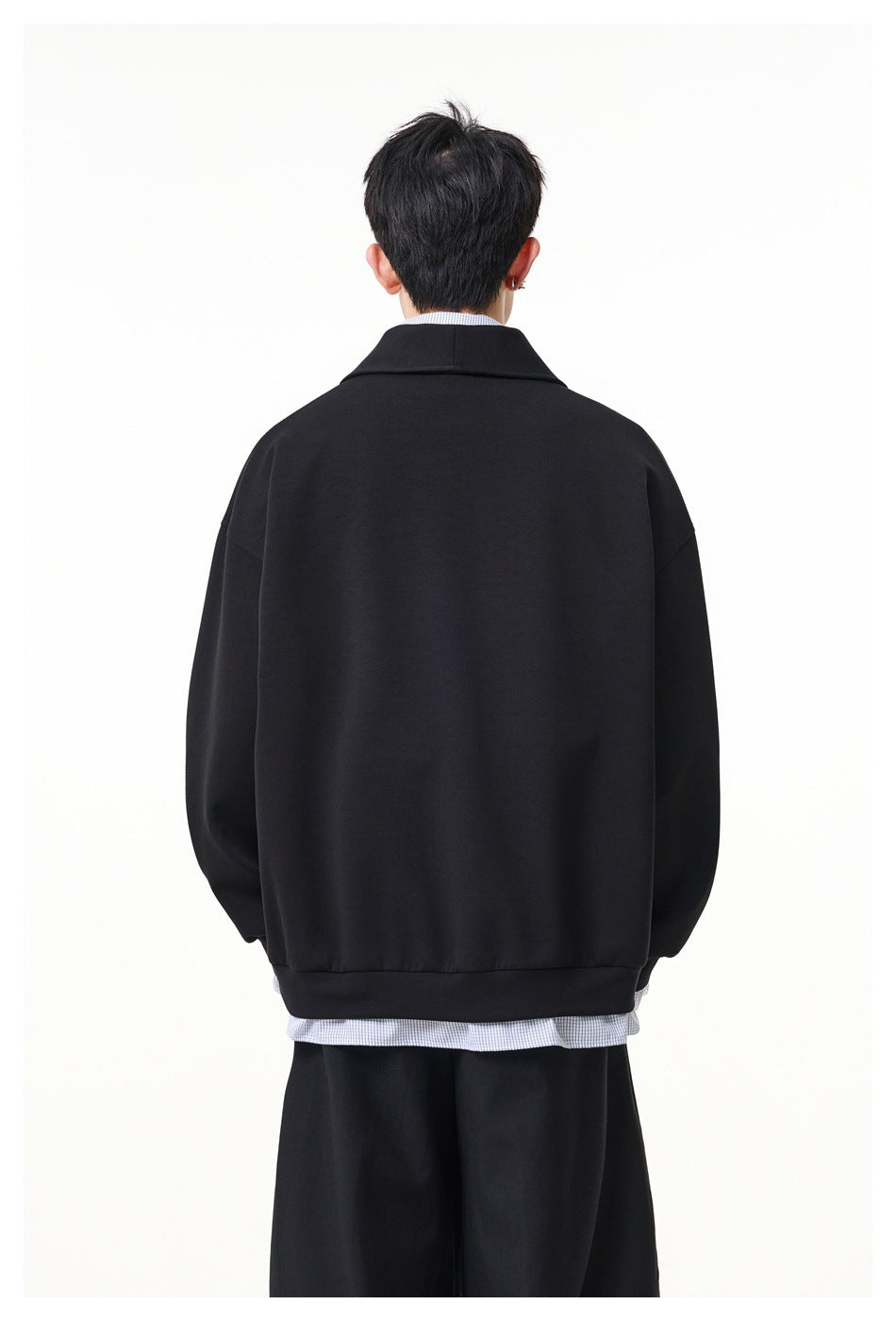 Rear view of a model wearing a black oversized pullover with a wide collar and ribbed hem.
