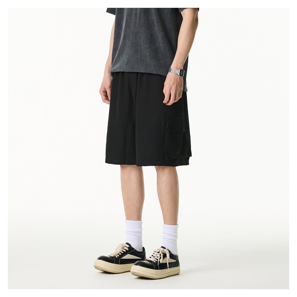 Side view of a model wearing loose black cargo shorts with a large flap pocket, a dark T-shirt, and sneakers.