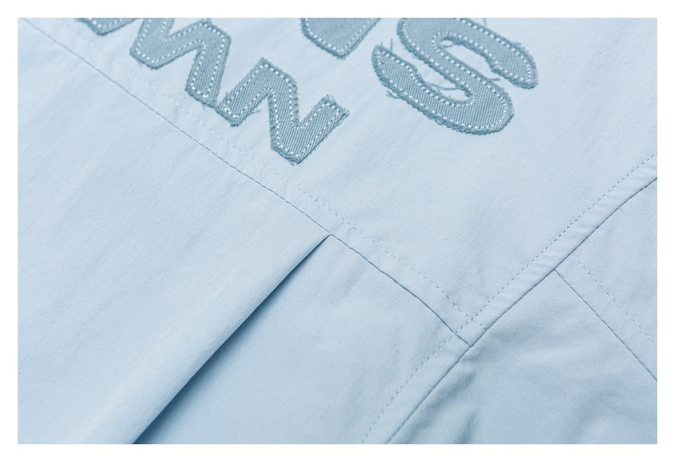 Close-up of embroidered English lettering and intersecting stitched seams on a light blue garment.