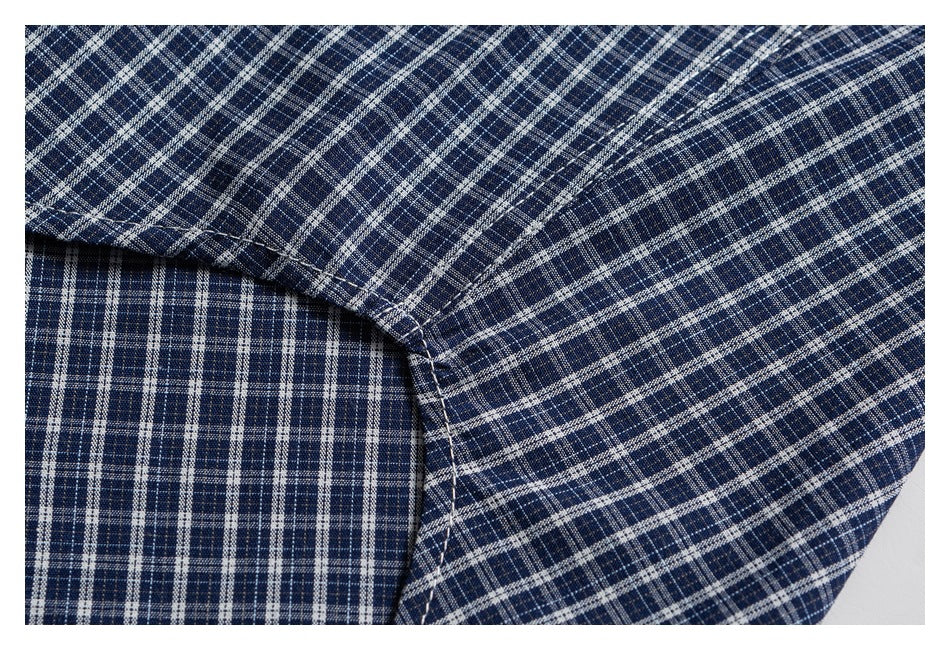 Close-up of a stitched garment seam on navy fabric with a fine white and gray plaid pattern.