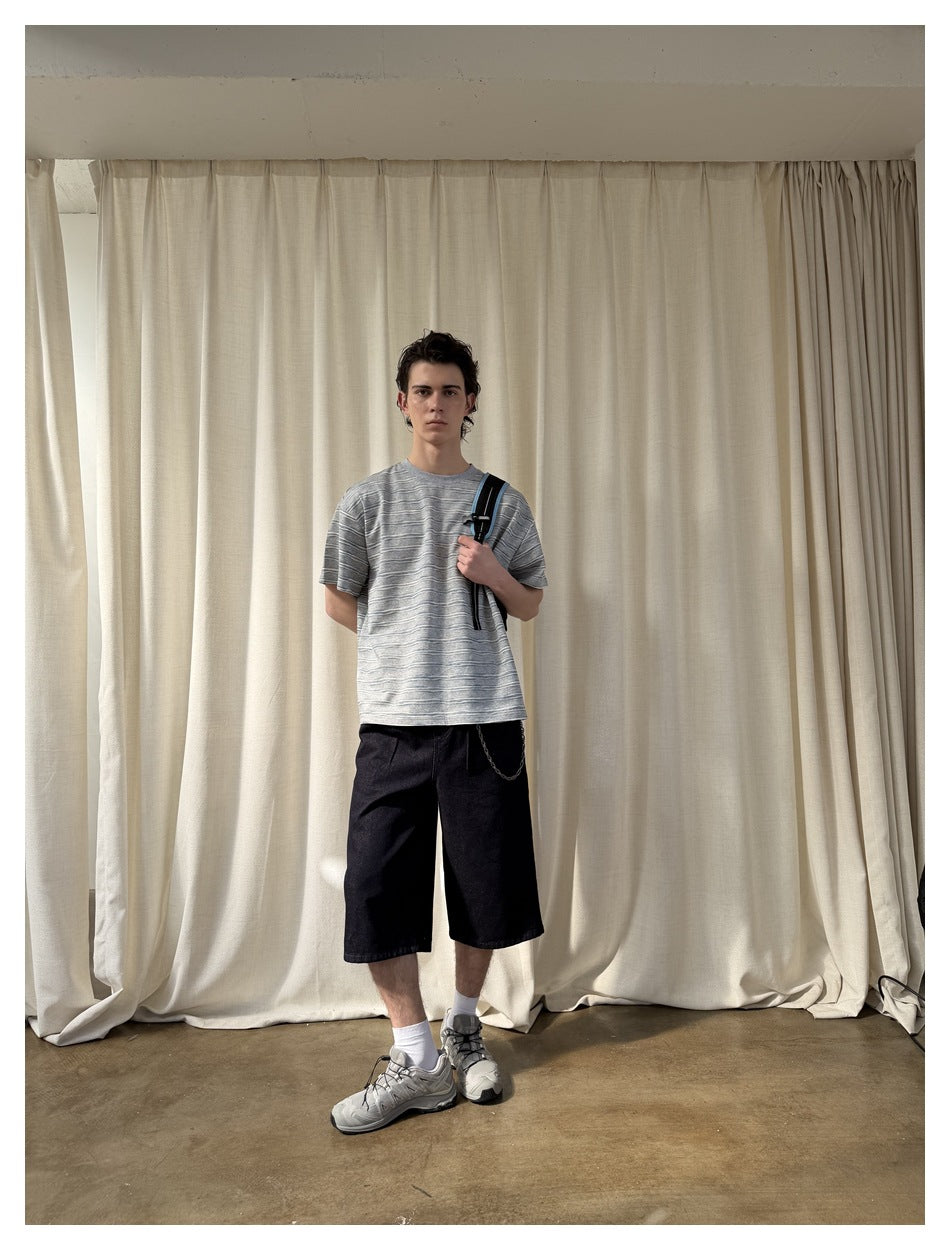Model facing forward in a gray horizontally striped T-shirt and black knee-length shorts, carrying a shoulder bag.