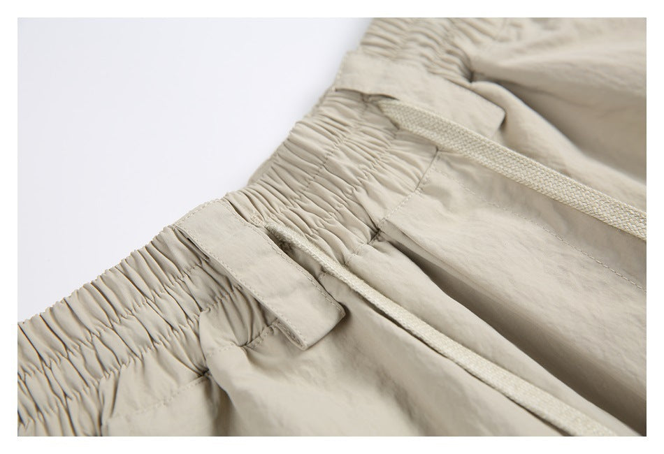 Close-up of light beige pants showing a gathered elastic waistband, drawstring, belt loop, and pocket seam.