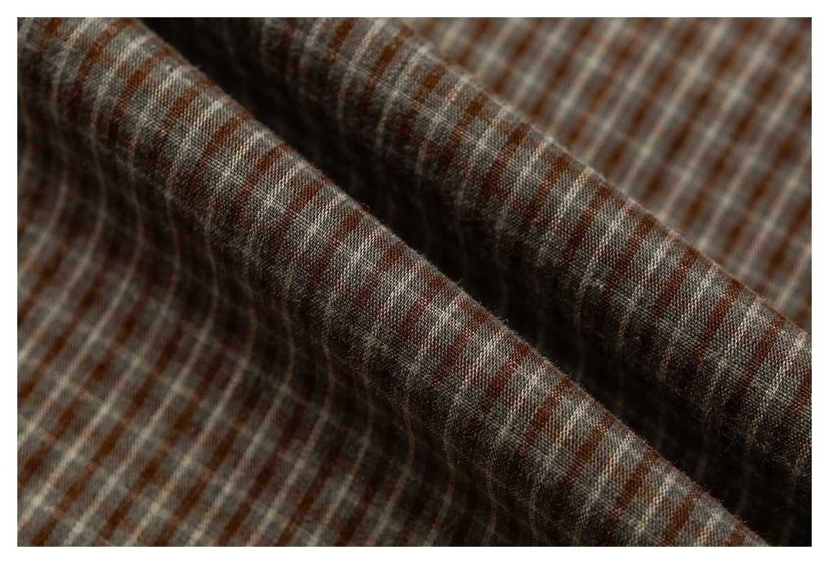 Close-up of brown, gray, and cream plaid fabric gathered into folds, showing its woven pattern and texture.