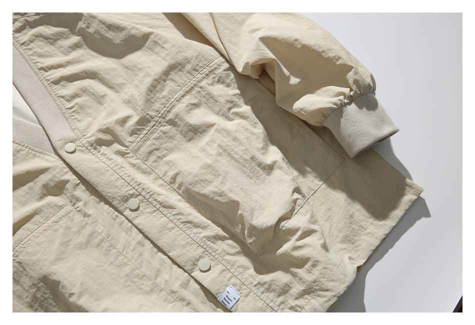 Close-up of the beige jacket’s snap front, large patch pocket, gathered sleeve, and ribbed cuff.