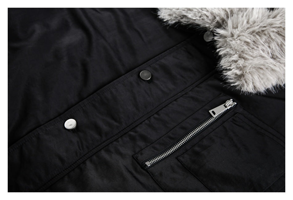 Close-up of a black coat showing snap buttons, a silver front zipper, a flap pocket, and gray fur trim.
