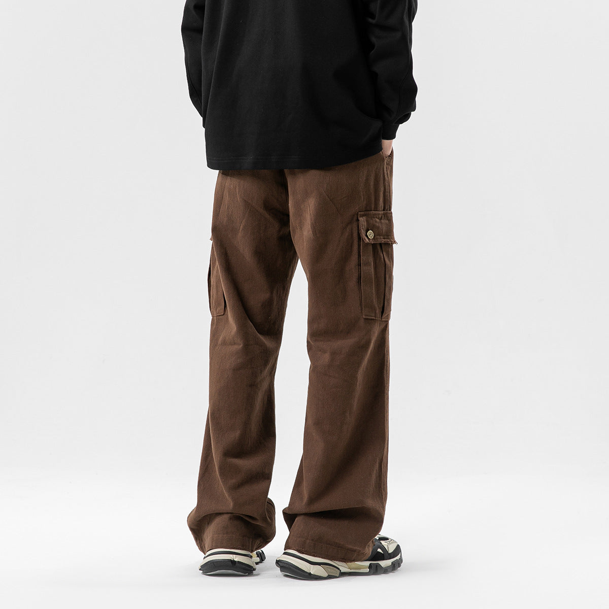 Rear view of a model wearing loose brown cargo pants with flap thigh pockets, a black top and sneakers.