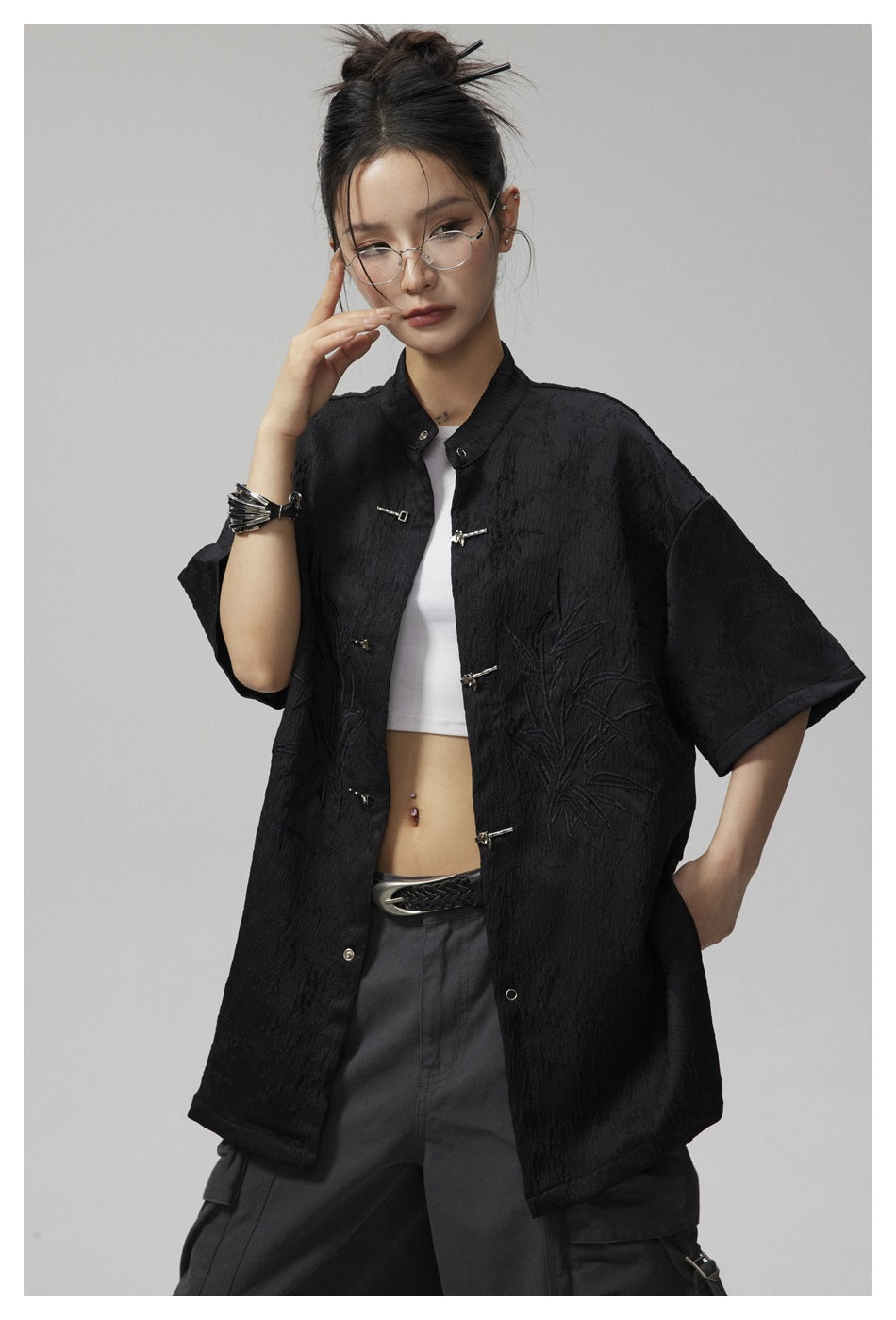 Model in a black short-sleeve jacket, shown close enough to see its metal frog closures and raised botanical embroidery.