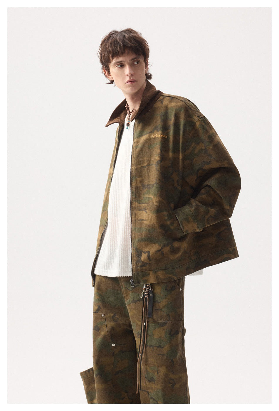 Model wearing a brown-green camouflage zip jacket with a dark collar and matching cargo-style trousers, shown from the front.