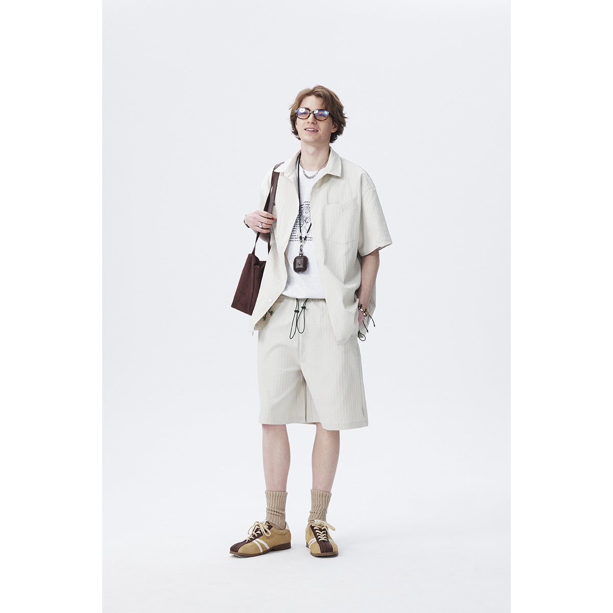 Model wearing an off-white short-sleeve button-up shirt and matching shorts over a graphic tee.