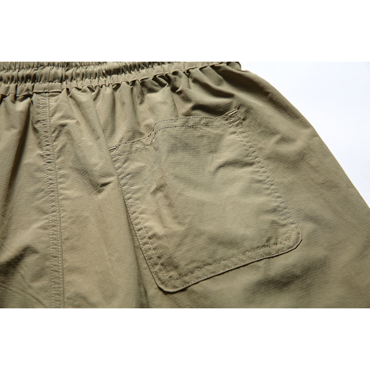 Close-up of the olive-khaki shorts' rear patch pocket and stitching below the elastic waistband.