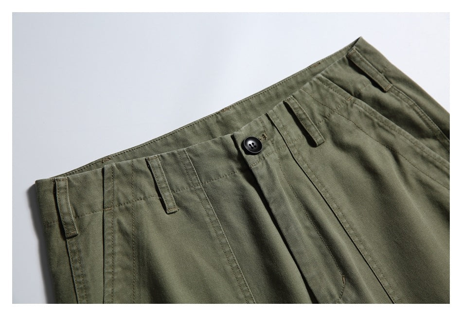 Close-up of olive-green trousers showing the front waistband, button, belt loops and pocket stitching.