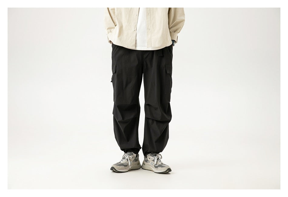Person wearing black cargo pants with knee pleats and ankle hems with a beige shirt and gray sneakers, front view