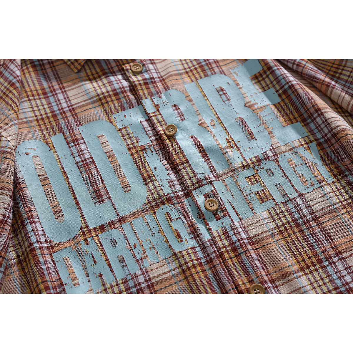 Close-up of a rust and tan plaid shirt with distressed light-blue “OLD RIDE” lettering and wooden buttons.