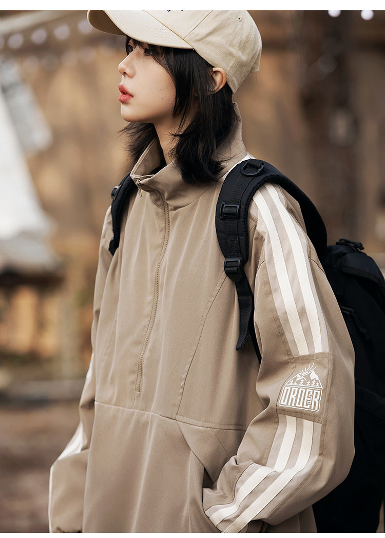 Close-up of the taupe jacket's cream sleeve stripes and embroidered graphic, with the short front zipper visible.