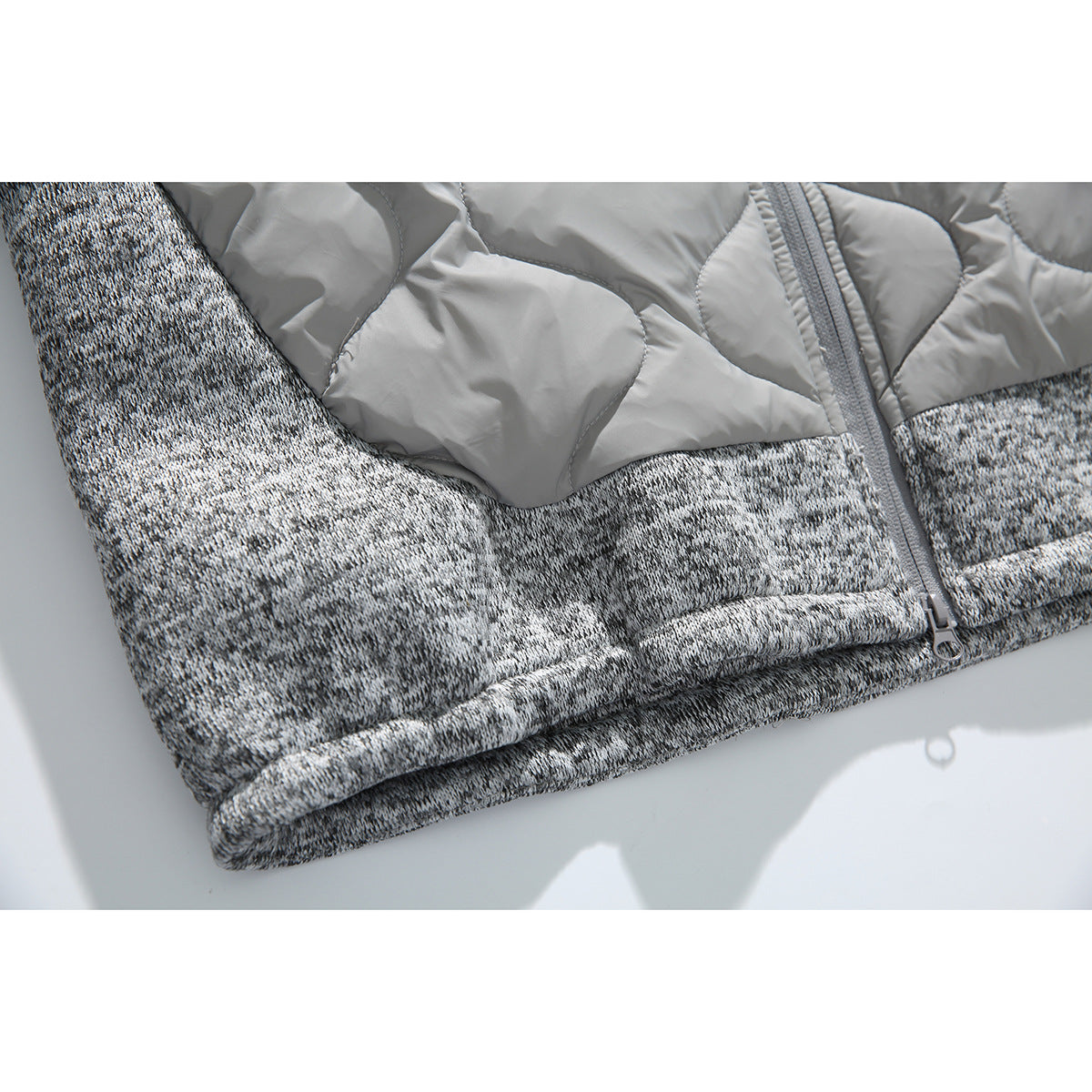Close-up of the gray jacket's quilted upper section, zipper, and mottled knit lower panel.