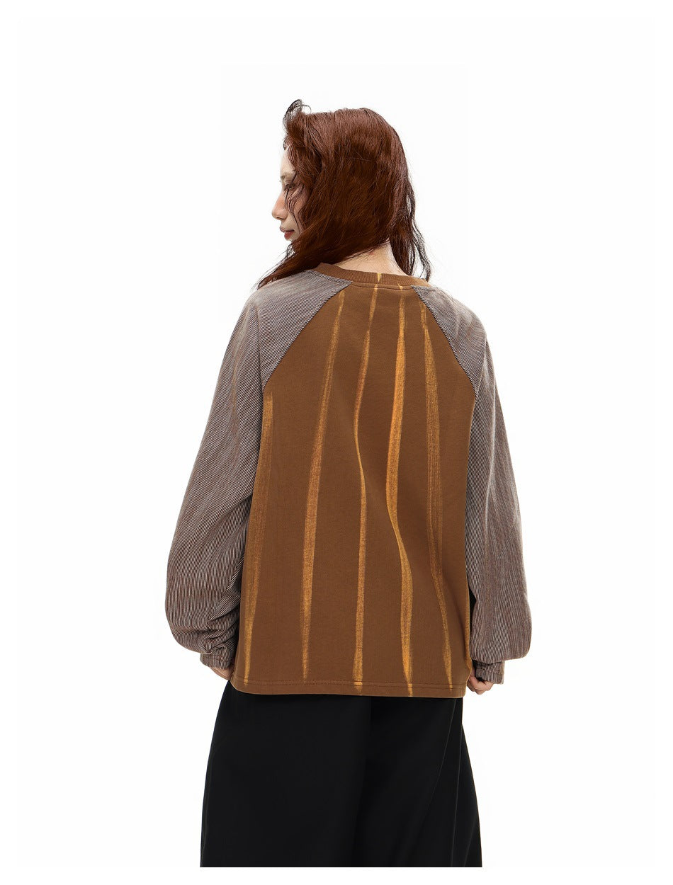 Back view of a model wearing a brown top with irregular gold vertical stripes and gray pinstriped raglan sleeves.