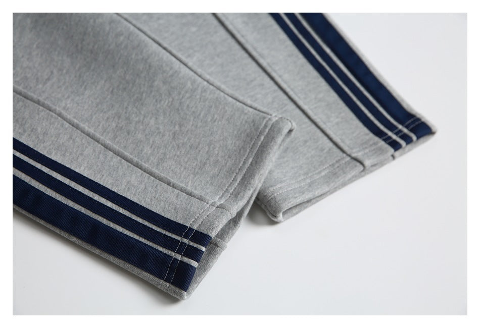 Close-up of gray sweatpants hems with navy side stripes and light accent stripes.
