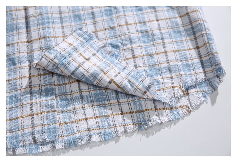 Close-up of a folded shirt sleeve and fringed hem on a light blue, gray, white, and tan plaid shirt.