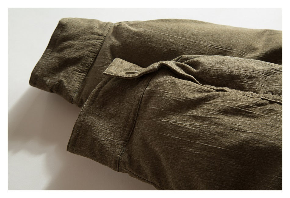 Close-up of olive-brown garment showing a wide stitched cuff and a small buttoned flap.