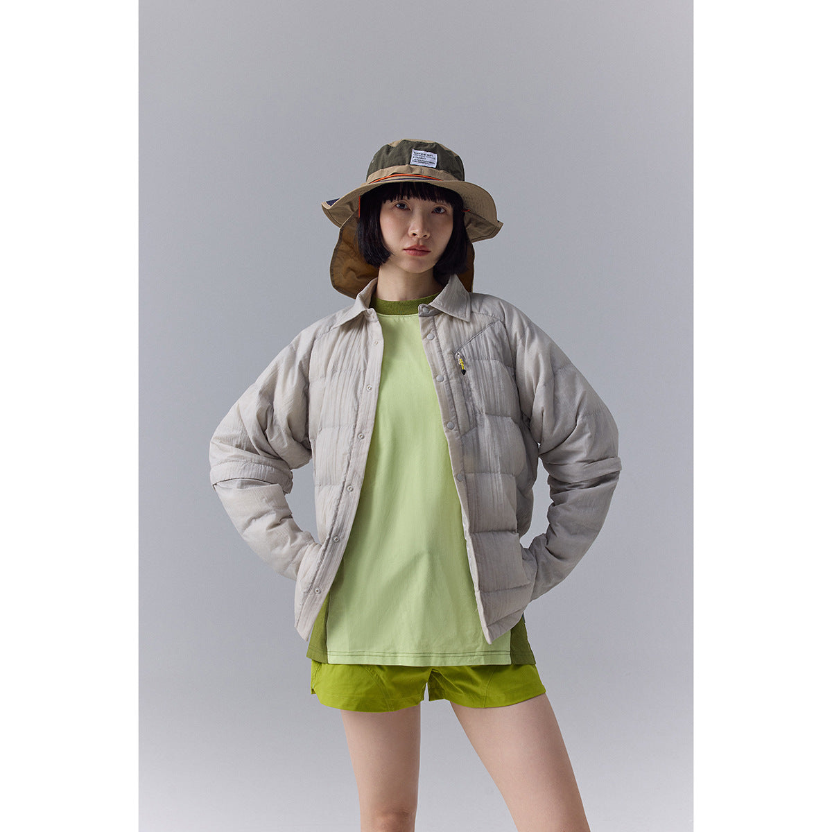 Front view of a model wearing a light gray quilted button-front jacket over a pale green shirt and lime shorts.