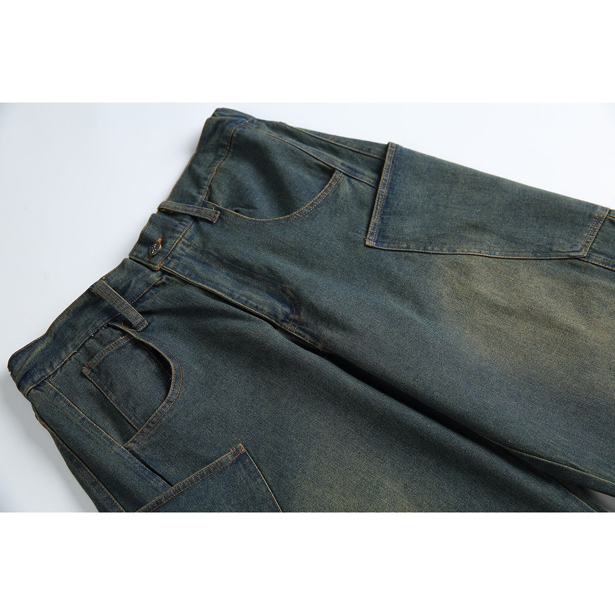 Close view of dark indigo jeans laid flat, showing the waistband, pockets, belt loops and orange contrast stitching.