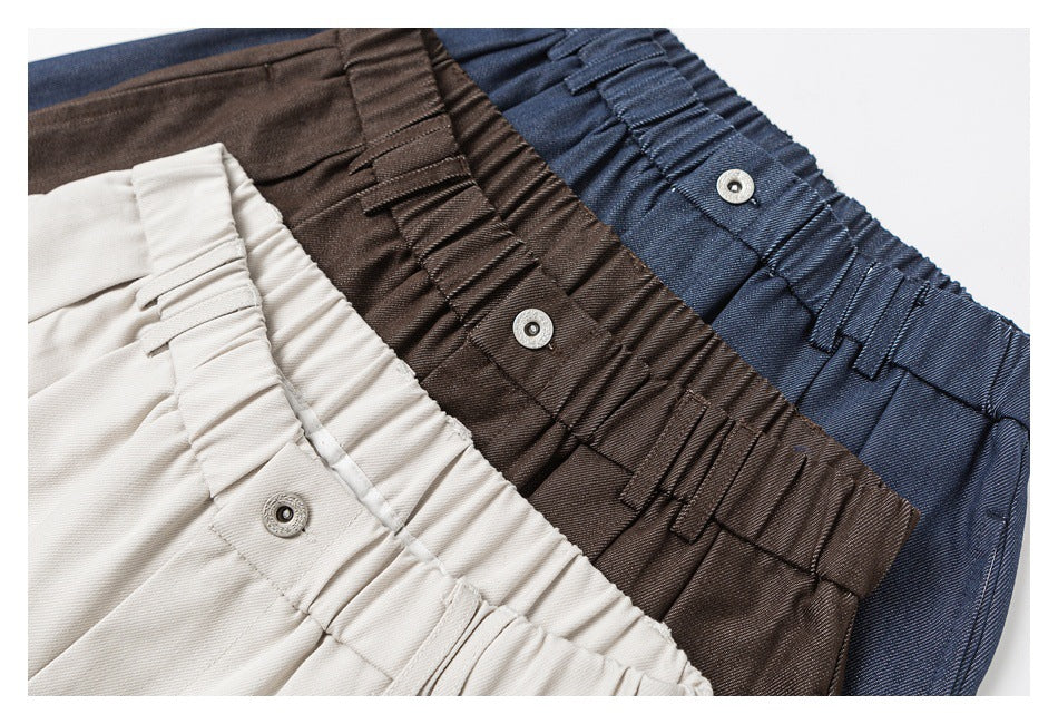 Close-up of elastic waistbands on trousers in ivory, brown, and navy, each with a metal button.