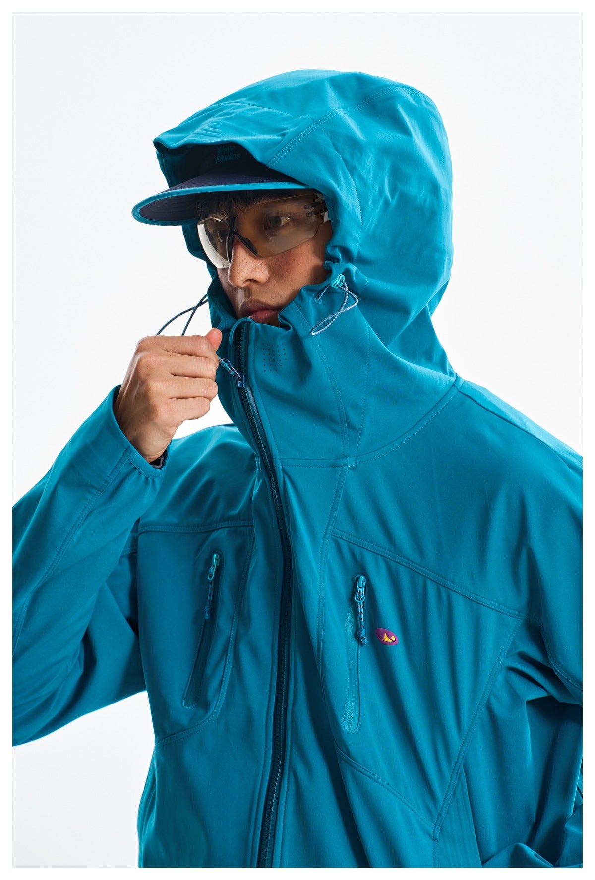 Close-up of the teal jacket's hood, high collar, drawcords, and chest zip pockets.