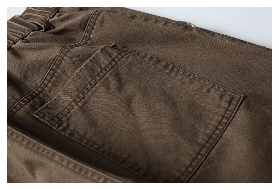 Close-up of brown trousers showing a rectangular rear pocket, waistband, and double-stitched seams.