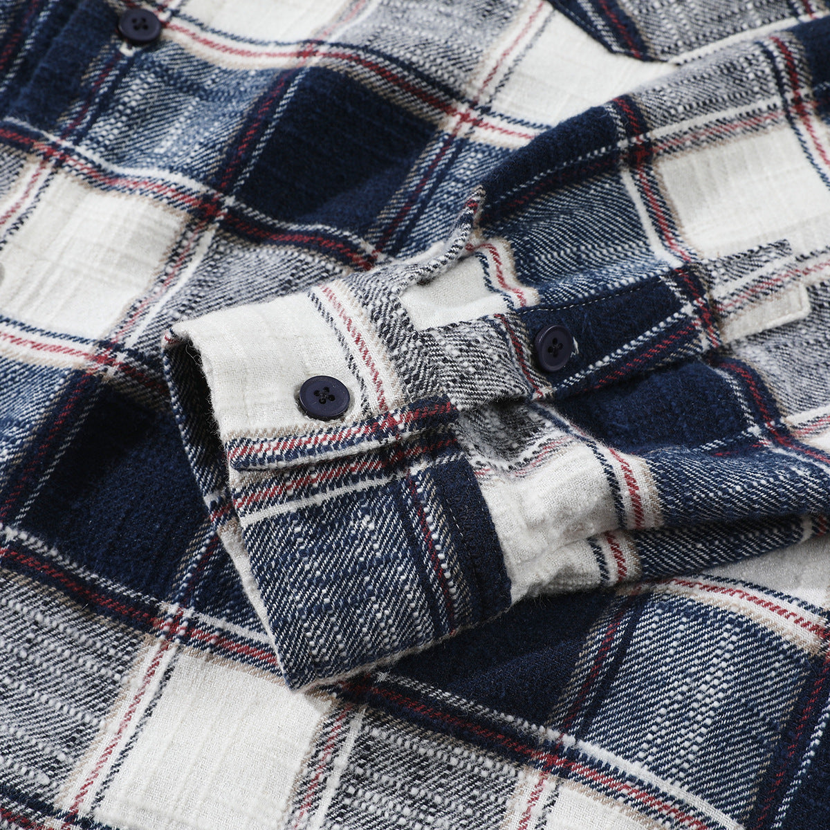 Close-up of a navy, white and gray plaid shirt cuff with thin red lines and dark buttons.