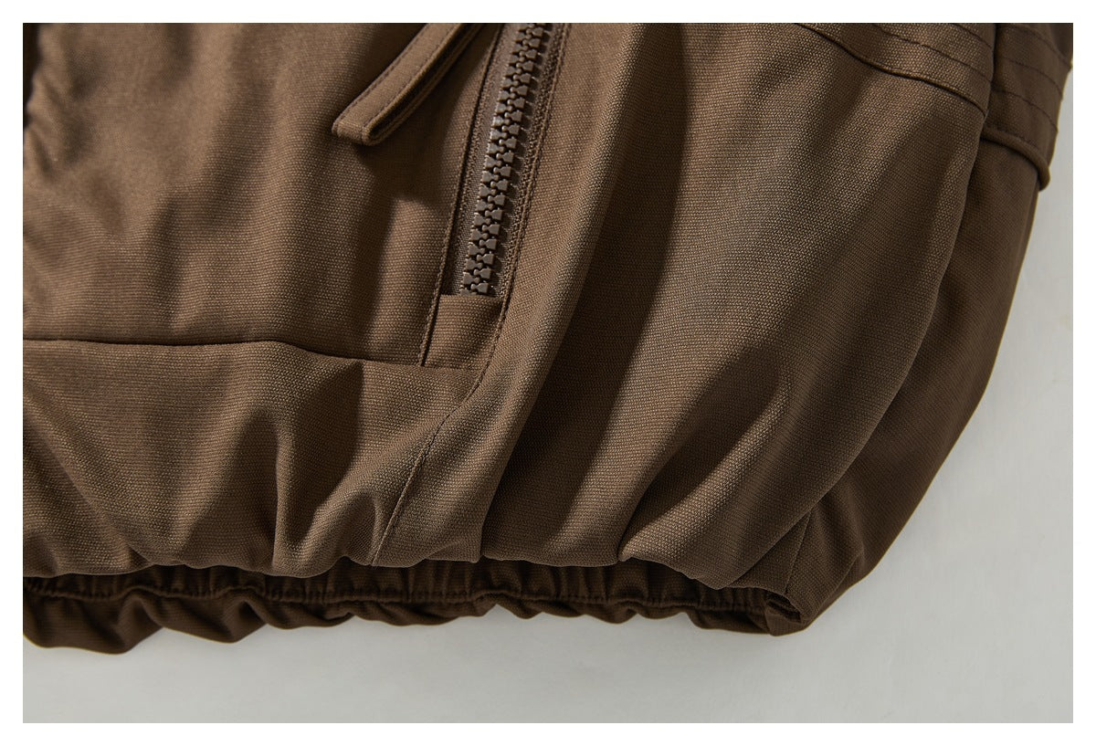 Close-up of a zippered pocket and gathered hem on a brown garment.