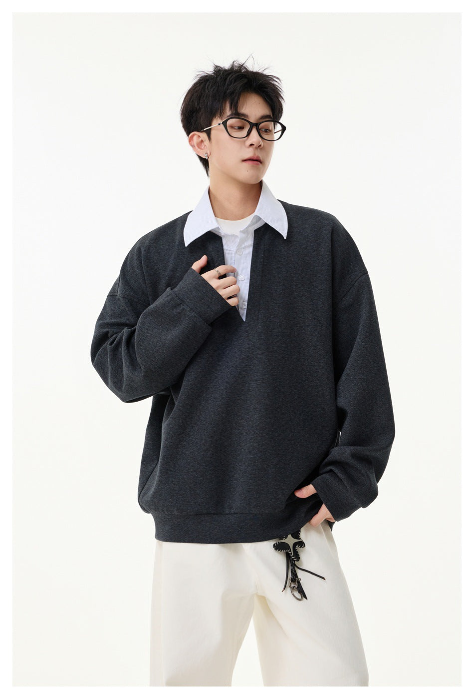 Model wearing a charcoal oversized V-neck sweatshirt over a white collared shirt, shown in a three-quarter view.