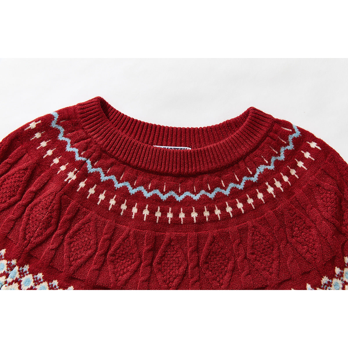 Close-up of a red crewneck sweater showing a blue-and-cream yoke pattern and raised cable-knit texture.