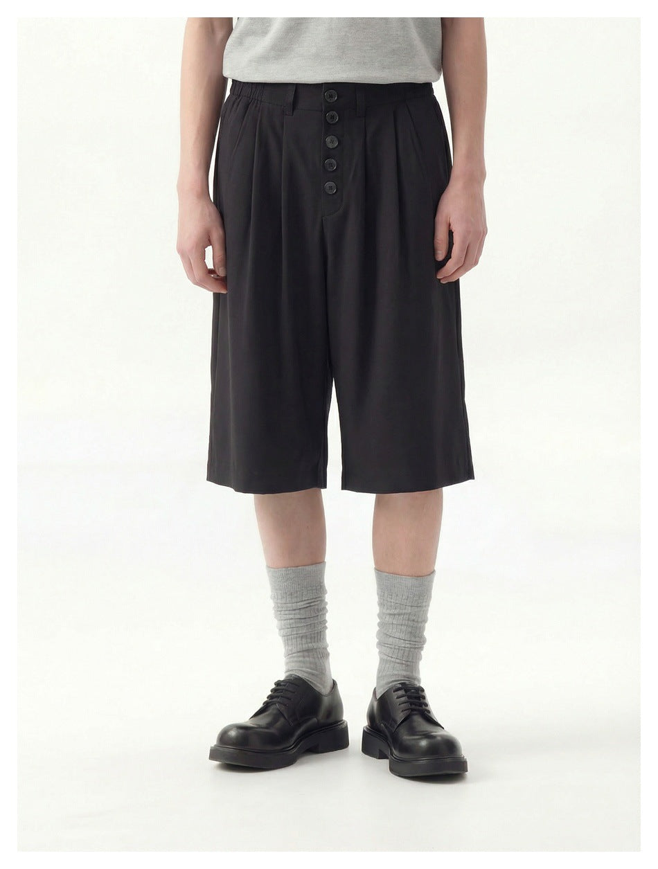 Model wearing black knee-length shorts with front pleats, a five-button fly and side pockets.