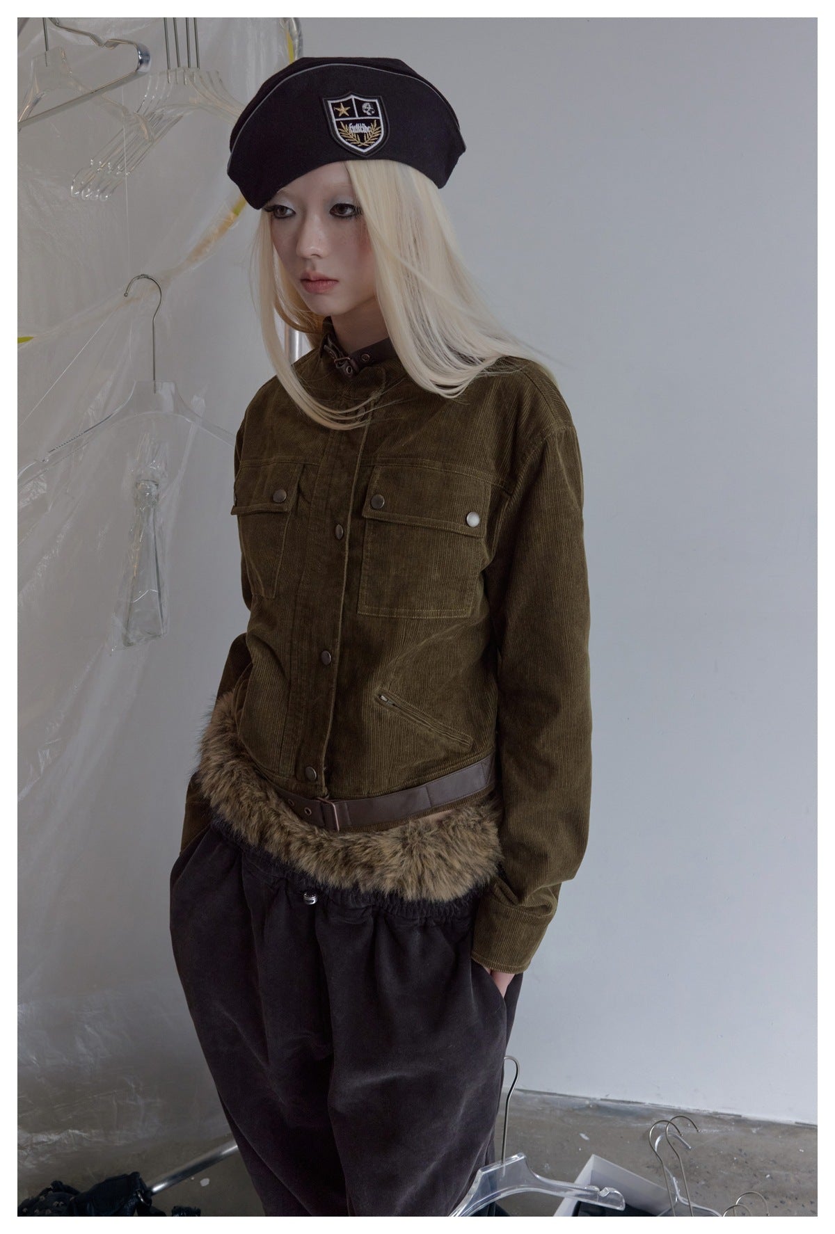 Model wearing an olive snap-front jacket with chest pockets, a brown belt and fur-trimmed hem.