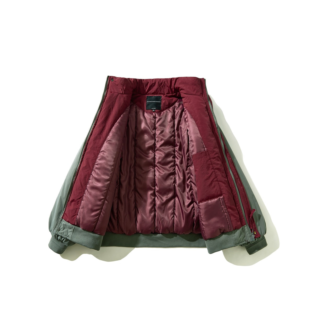 Sage green jacket opened to show its burgundy quilted lining and inner label.