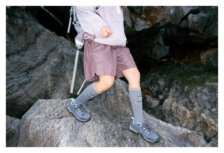 Hiker in mauve shorts and a pale jacket striding across rocks, shown from the front at waist level.